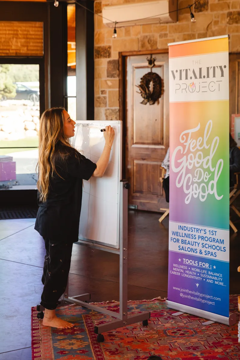 Elizabeth Faye teaching at a whiteboard beside a Vitality Project banner