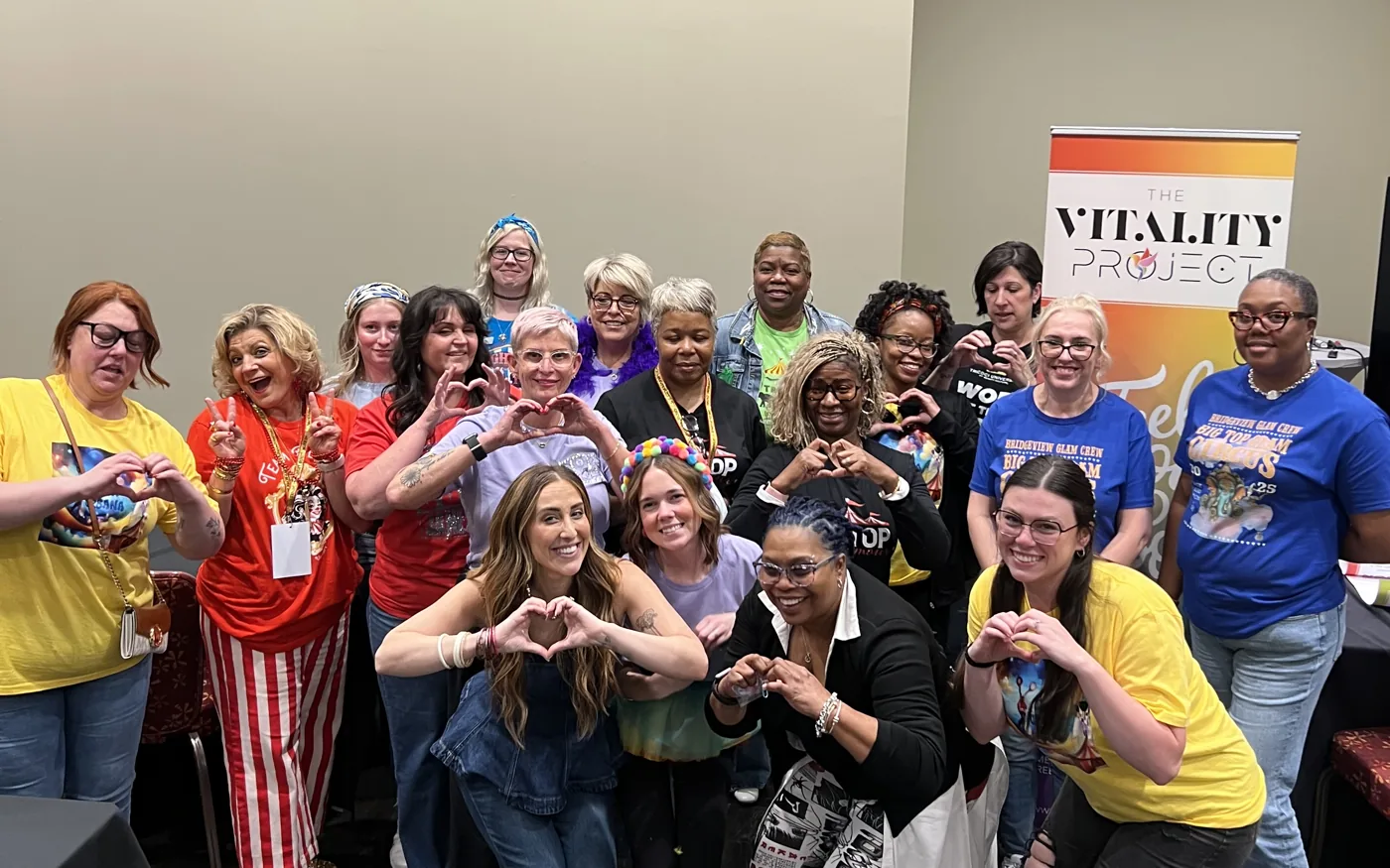 A school team making hearts with their hands beside a Vitality Project banner