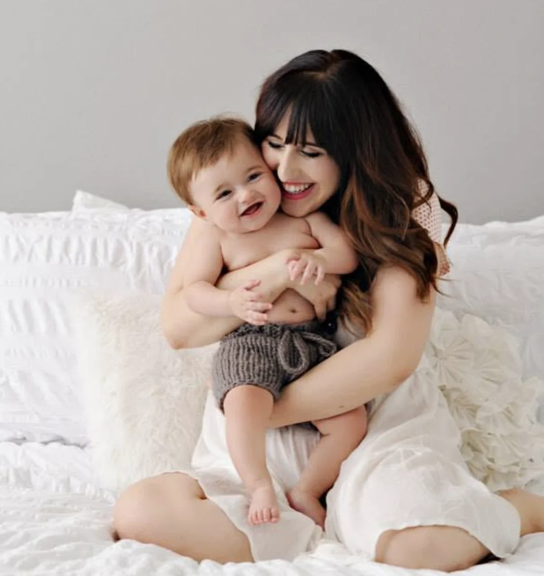 Elizabeth Faye laughing with her baby son on a white bed