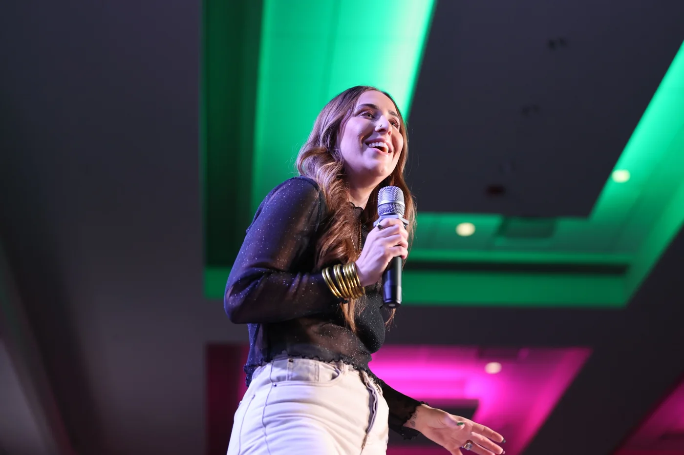 Elizabeth Faye on stage with a mic, giving a keynote under green and pink lights